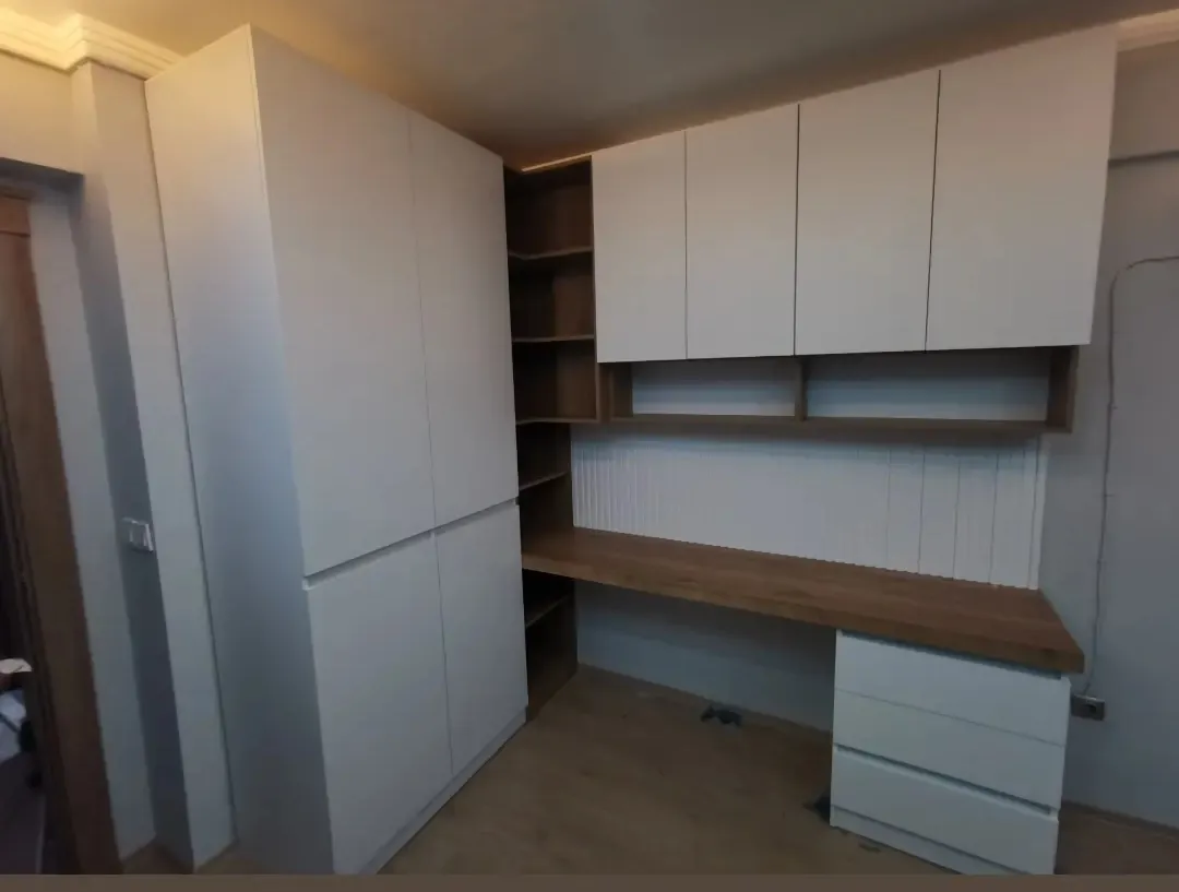 Beyaz kapaklı genç odası dolabı; ahşap tonlu çalışma masası, köşe raflar ve çekmeceli modül